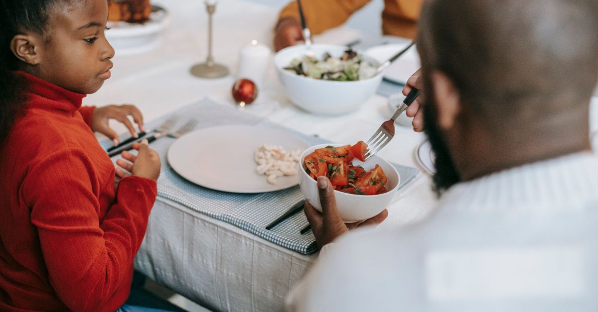 Thoughtful African American girl expecting salad in plate with forks placed on festive table