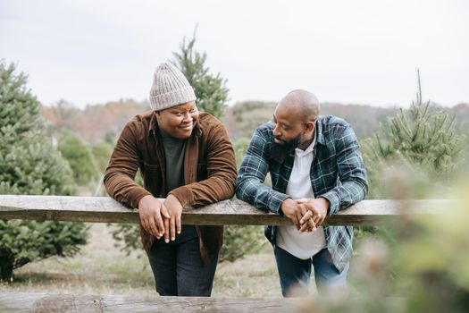 African American teen man having conversation with dad leaning on fence standing against green trees and looking at each other