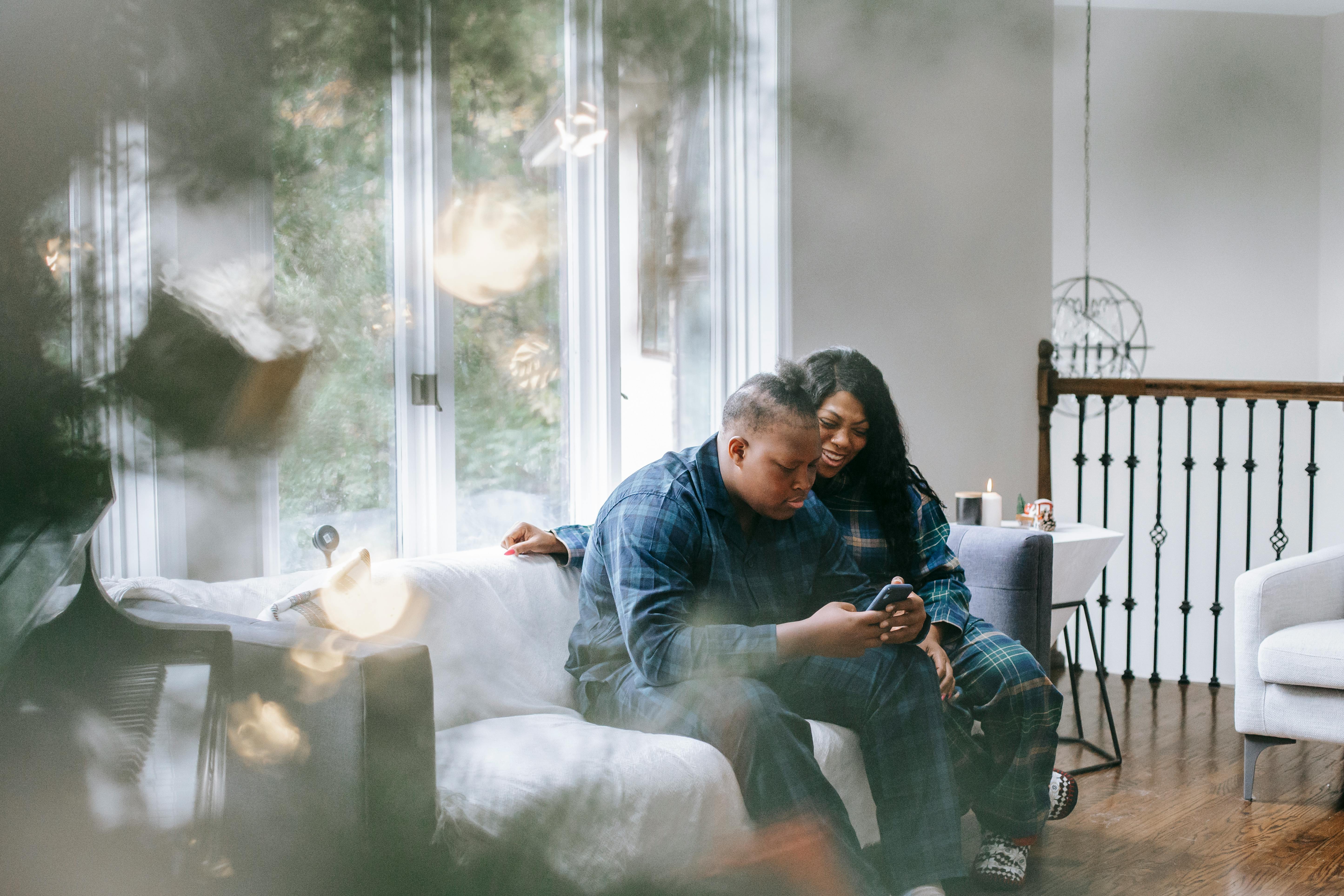 focused black teen son watching smartphone while sitting with mother