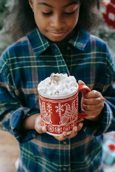 A young girl holds a festive mug of hot chocolate topped with whipped cream, perfect for holiday warmth.