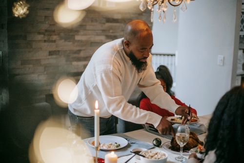 Free African American man cutting chicken placed on served table with assorted food and wine with burning candles Stock Photo