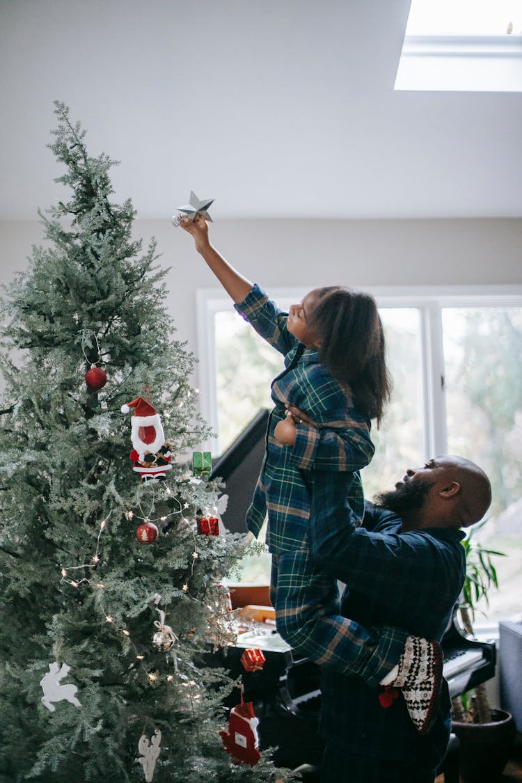 A Girl Putting A Star On Top Of A Christmas Tree