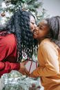 Side view of smiling African American mum kissing cheerful daughter while giving Christmas gift box