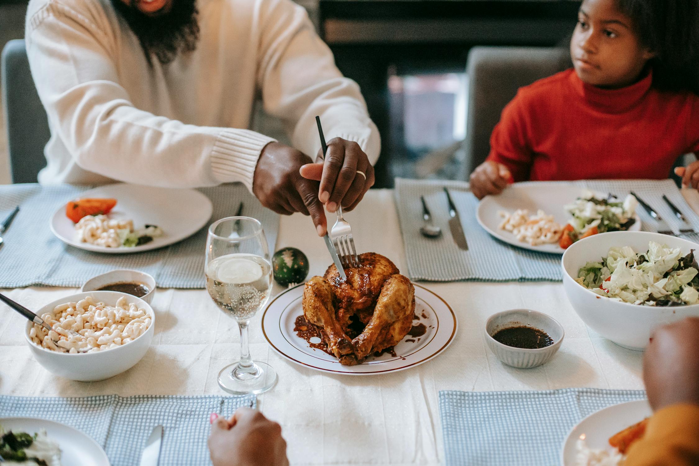 A family sits at the dinner table with multiple dishes in the foreground. Someone is extending their arms to carve the turkey in the middle. Photo by pexels user Any Lane. Photo used courtesy of Pexels.com.