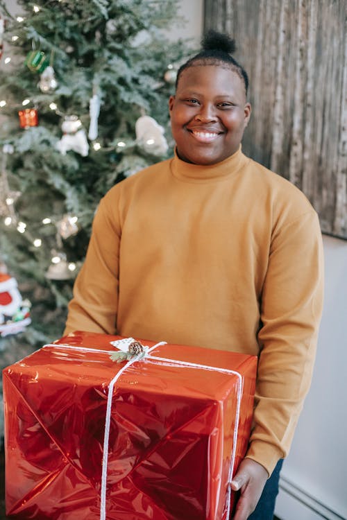 Happy black teen with present box near Christmas tree