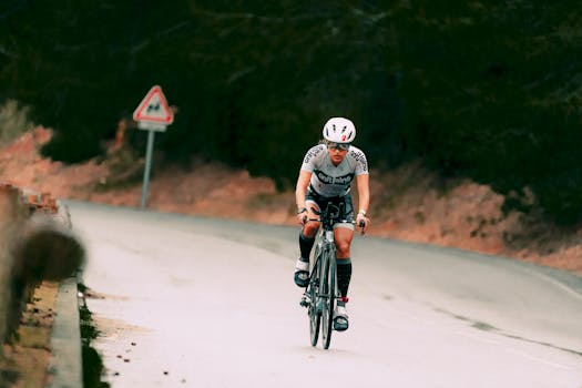 Full body of faceless person in t shirt and helmet riding bicycle on asphalt road in daytime on blurred background