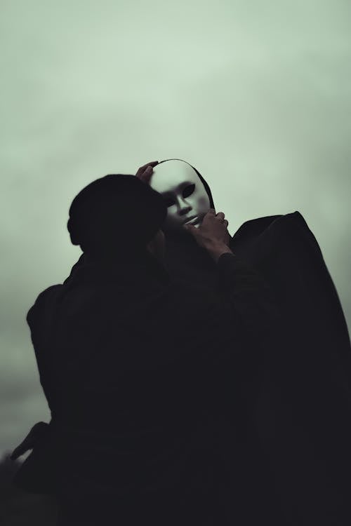 Black and white of anonymous male in black outfit covering face of faceless person with white mask