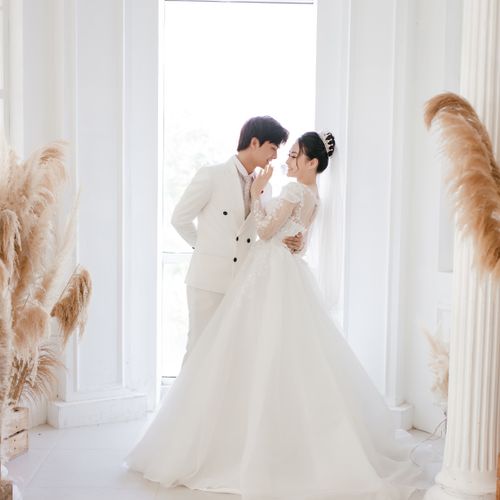 Free Side view full body gorgeous Asian bride touching grooms lips while embracing together in light wedding studio and looking at each other with love Stock Photo