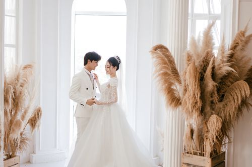Free Side view positive newlywed Asian couple wearing classy gowns holding hands and dancing in fancy wedding studio Stock Photo