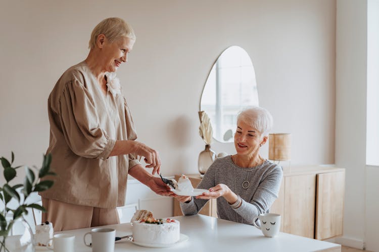 An Elderly Woman Giving Cake To Her Friend