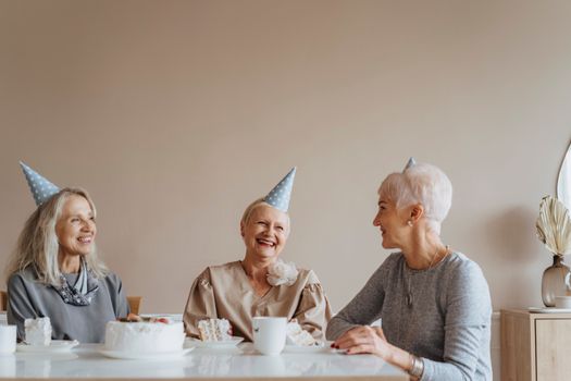 三位年长的女士头戴派对帽，在舒适的室内微笑着享受生日庆祝活动