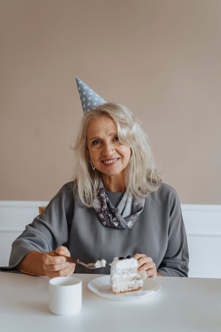 Photograph Of An Elderly Woman With A Party Hat Eating Cake