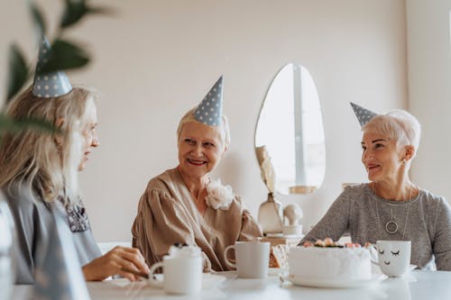 Photograph of Elderly Women with Party Hats Having a Conversation