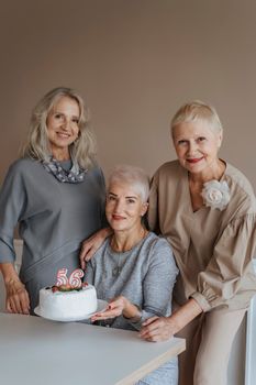 三位年长女性在室内拿着蛋糕庆祝生日，洋溢着幸福与友谊