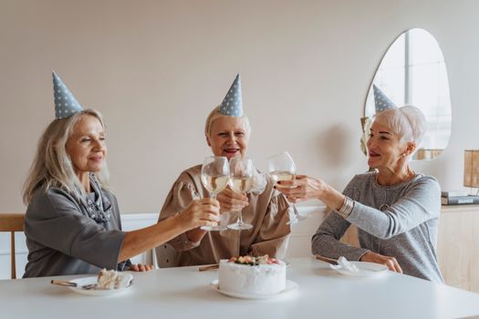 三名资深高加索妇女在室内用香槟和蛋糕庆祝生日