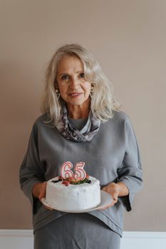 一位快乐的老年妇女在室内拿着插有65根蜡烛的蛋糕庆祝生日