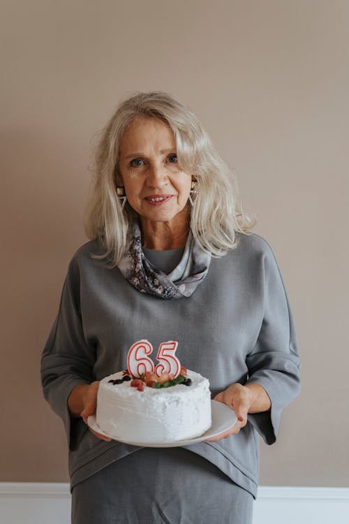 An Elderly Woman Holding a Plate with a Birthday Cake