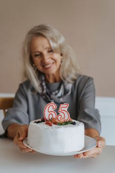 一位快乐的老年妇女在室内用水果蛋糕庆祝她的65岁生日