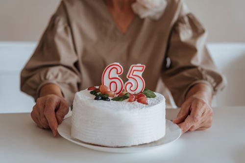 Free Elegant 65th birthday cake with candles and fruit garnishes. Stock Photo