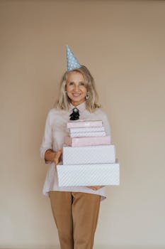 Senior woman in party hat holding gift boxes, smiling joyously indoors.