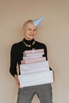 一位资深女士在室内头戴派对帽，兴高采烈地捧着一堆礼物