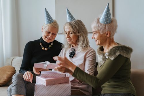 Free Three senior women enjoy a birthday celebration with gifts and party hats indoors. Stock Photo
