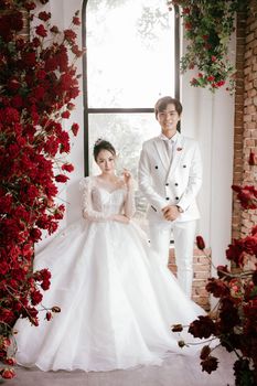 一对亚洲夫妇身着优雅婚纱，在鲜花盛开的房间里