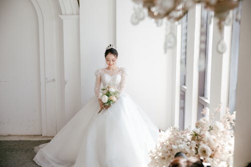 Happy ethnic bride in dress and crown with bouquet