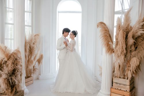 Free Full body side view of ethnic couple wearing gorgeous wedding outfits hugging while standing near arched window Stock Photo