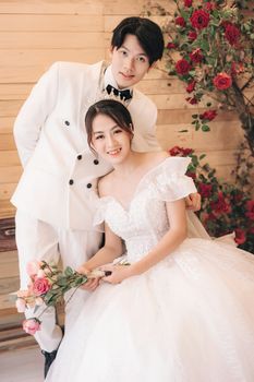 Beautiful portrait of an Asian couple on their romantic wedding day, surrounded by roses indoors.