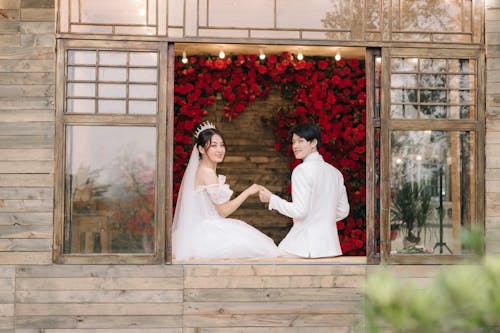 Bride and Groom Sitting on a Windowsill and Holding Hands 