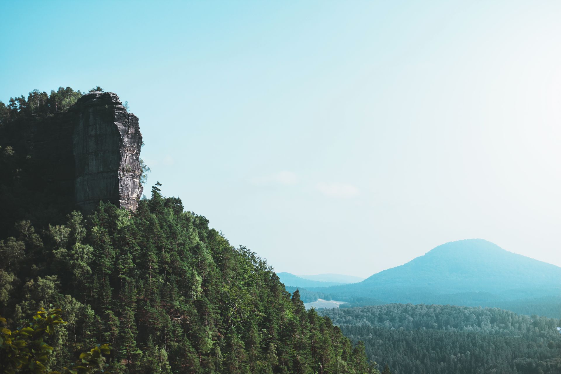Serene landscape of a mountain with lush green forest under a clear, bright sky.