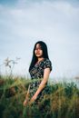 阳光明媚的一天，一位身穿花卉连衣裙的亚洲女子在宁静的草地上摆着姿势