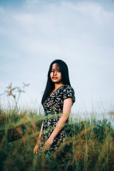 阳光明媚的一天，一位身穿花卉连衣裙的亚洲女子在宁静的草地上摆着姿势