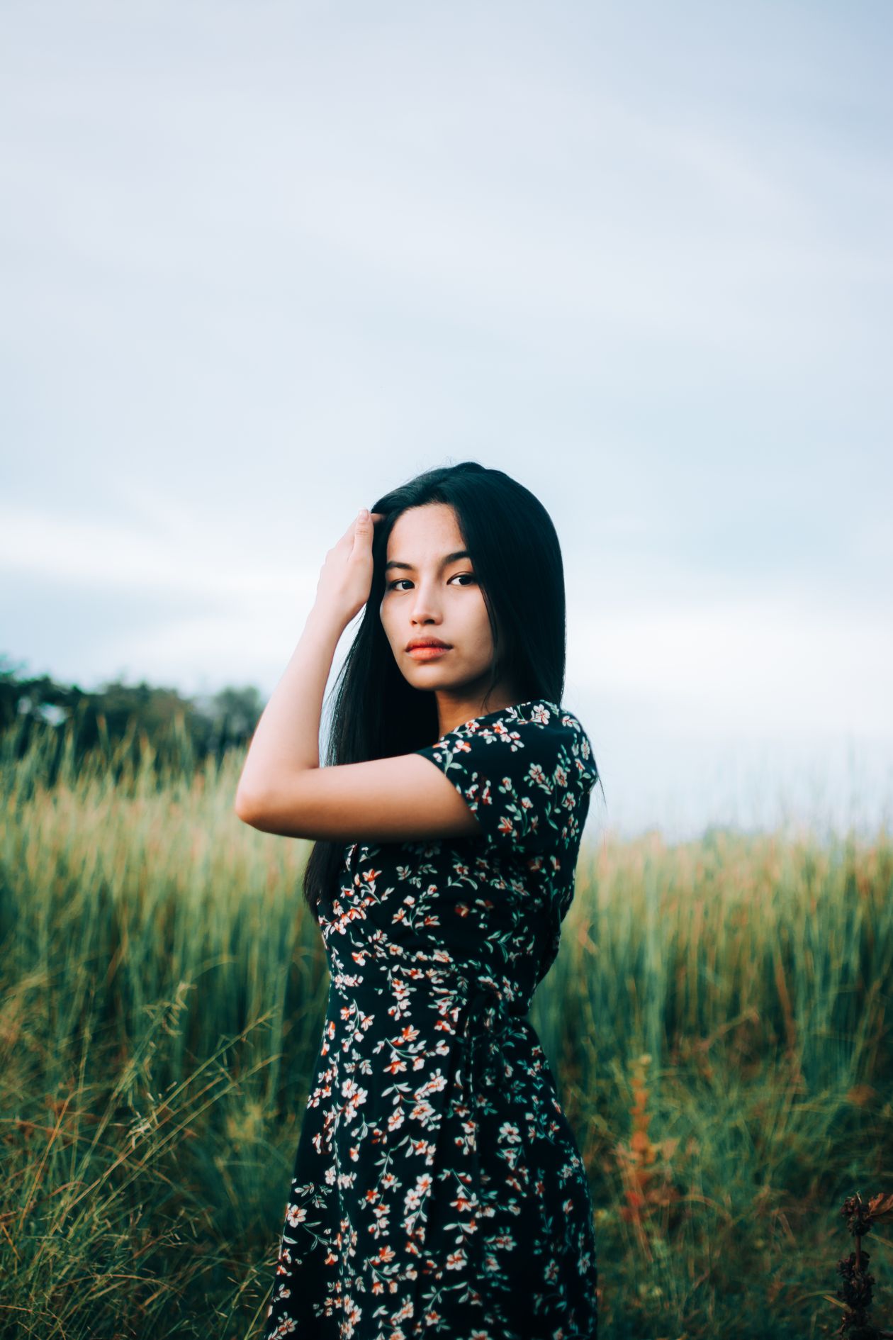Woman in a dark floral dress standing in a grassy field