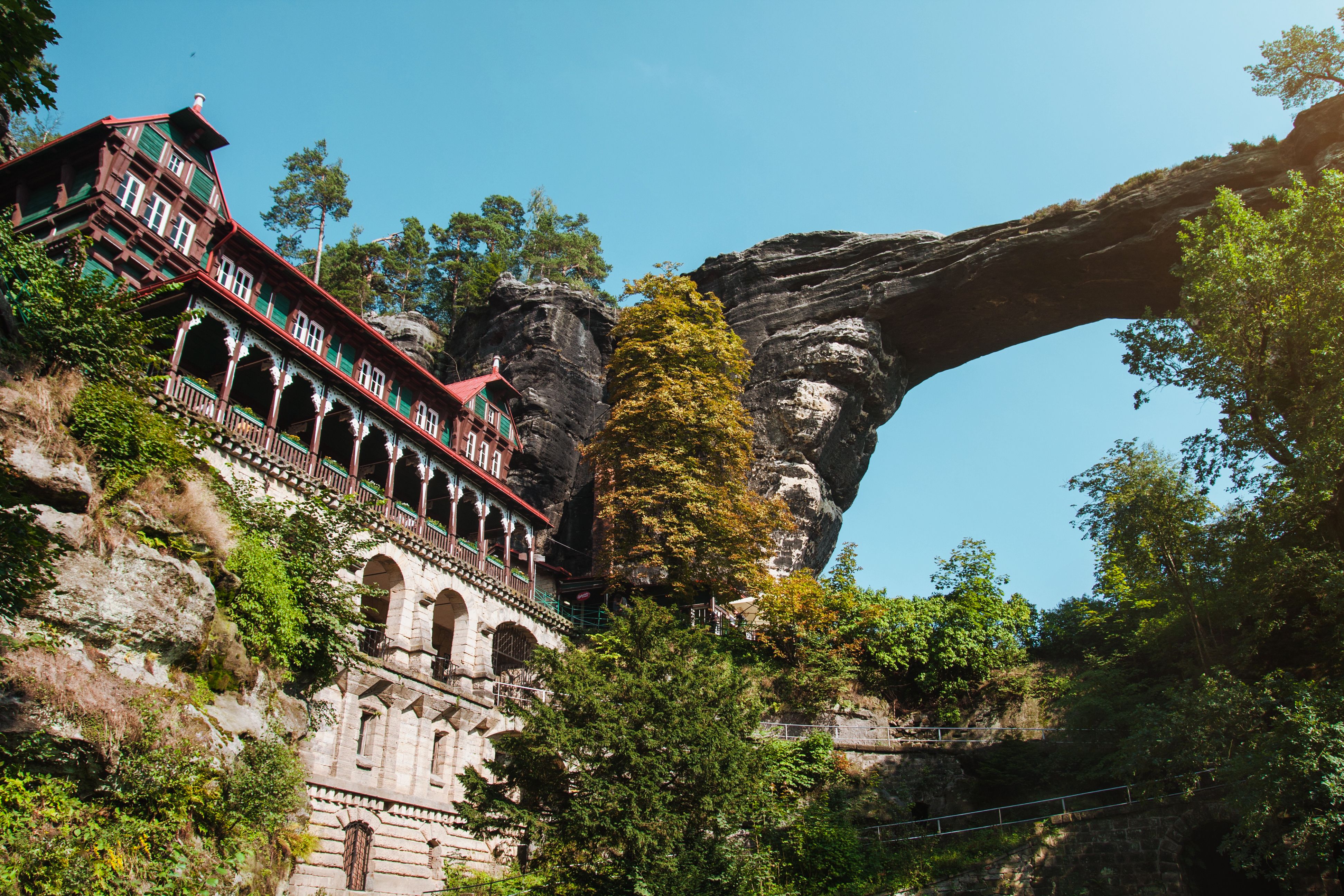 Pravčická Gate at golden hour with sandstone formations, forest backdrop, and panoramic views of Bohemian Switzerland National Park glowing in warm morning light