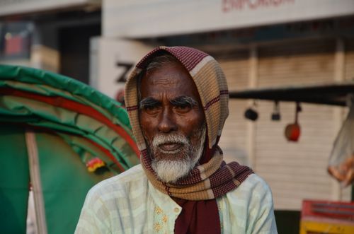 Free Portrait of an elderly man wearing a headscarf in a bustling outdoor environment. Stock Photo