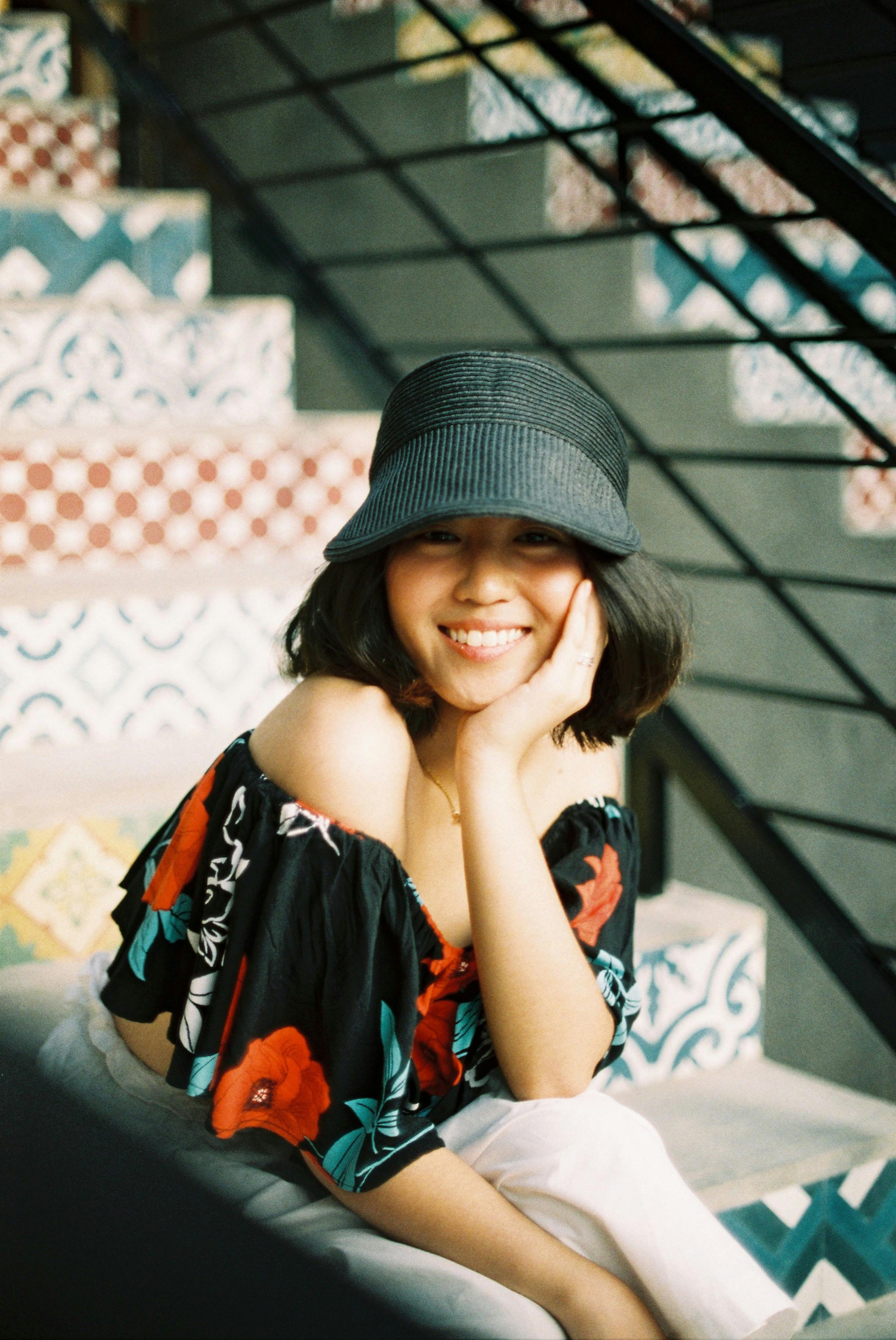 A young woman with a black hat smiles while sitting on colorful mosaic steps.