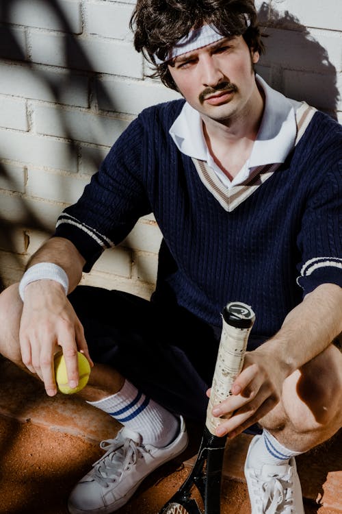 Man Resting while Holding a Tennis Racket and Ball