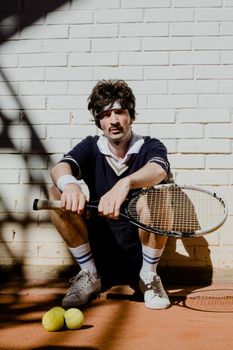 Stylish man in vintage tennis attire with racket and balls outdoors.