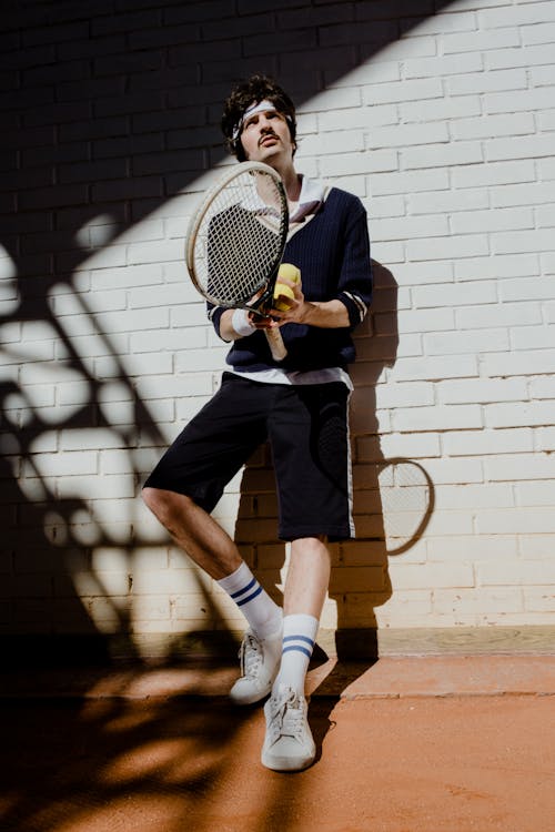 A Man Leaning on the Wall Holding Tennis Racket