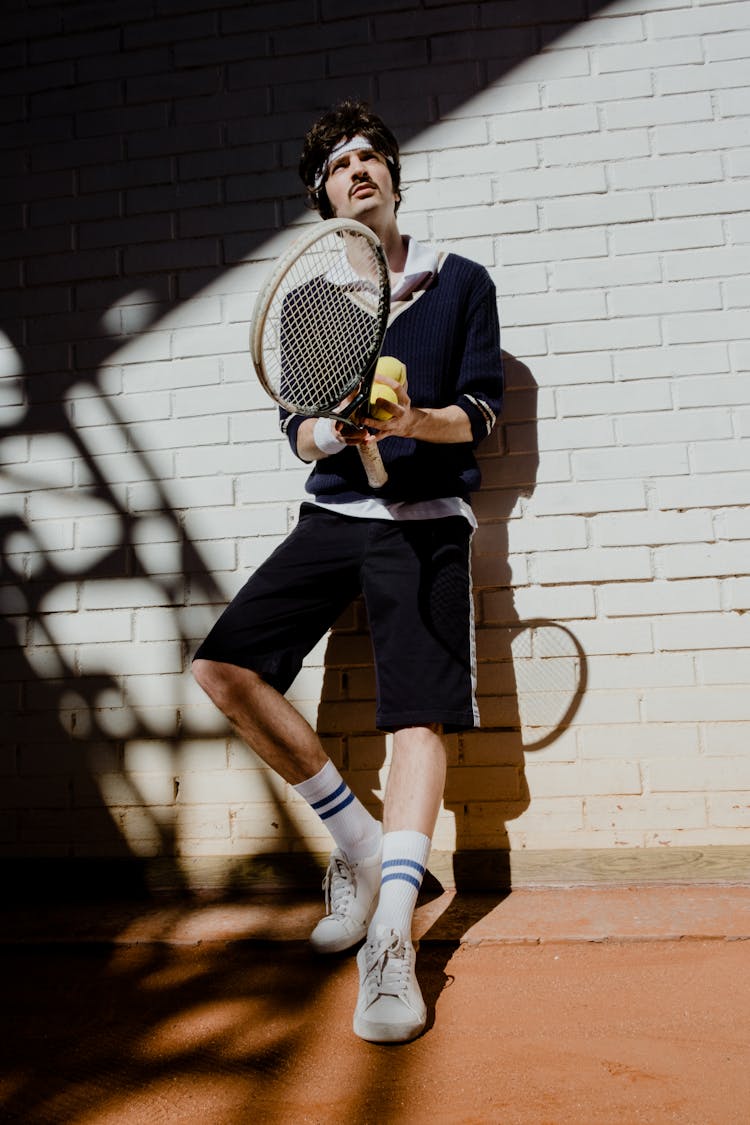 A Man Leaning On The Wall Holding Tennis Racket