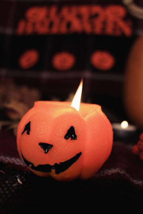 Free Orange jack-o'-lantern candle glowing warmly, perfect for Halloween decorations indoors. Stock Photo
