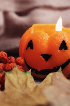 A lit jack-o-lantern candle surrounded by fall leaves and berries, embracing Halloween spirit.
