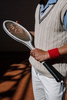 Portrait of a tennis player in classic attire holding a vintage racket indoors.