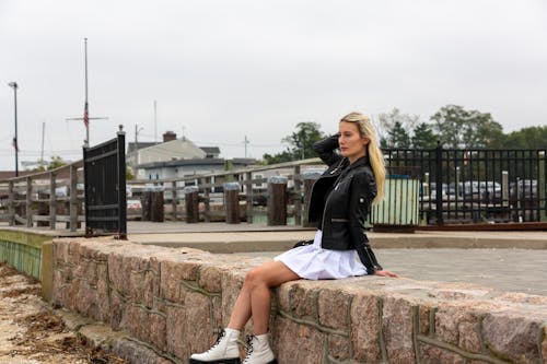 Side view of young female with long hair in leather jacket and skirt looking away while resting on parapet