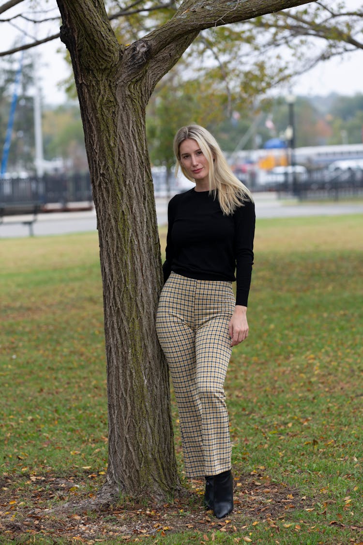 Woman In Trendy Checkered Trousers Near Tree On Green Lawn