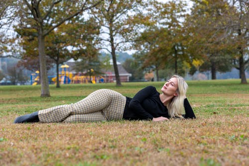 Free Full body of female with long fas hair and eyes closed in trendy checkered trousers relaxing on lawn with grass Stock Photo