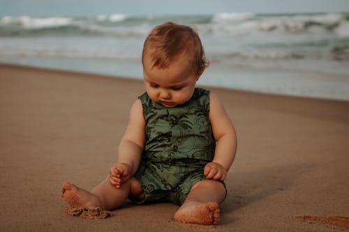 Cute baby in ornamental wear resting on sandy sea shore