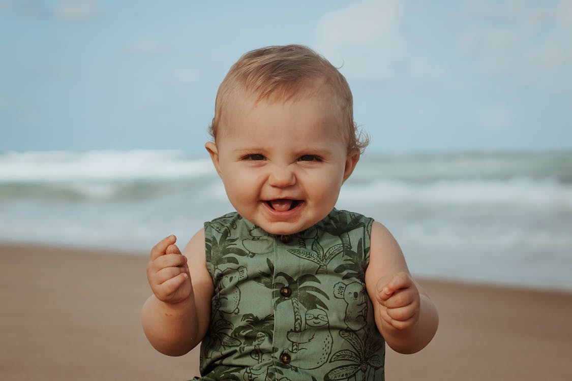 Cheerful baby on sandy sea shore in stormy weather